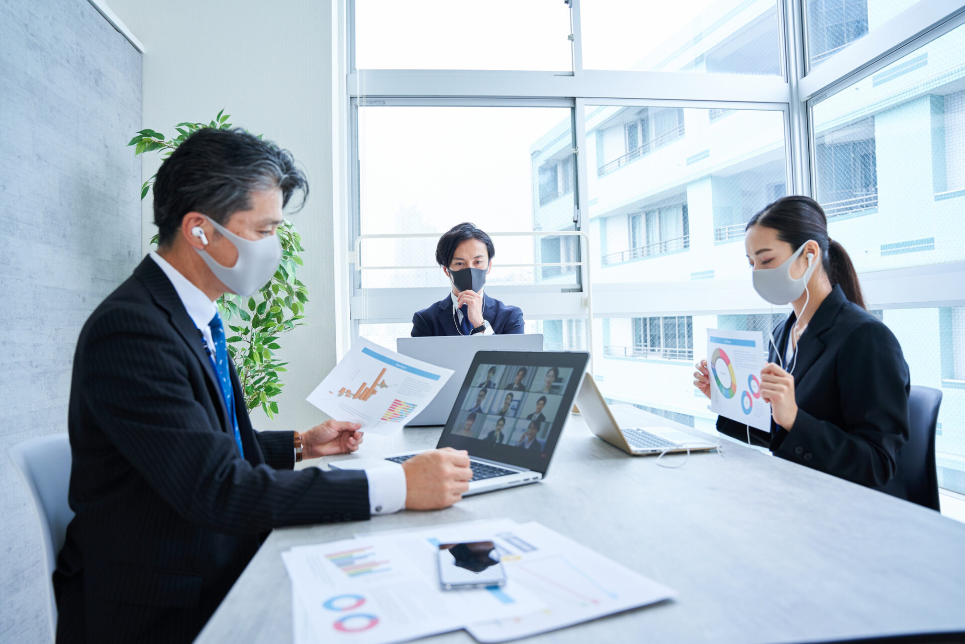 ハイブリッドワークのオンライン会議でマスクを着用して資料を投影しているオフィス出社の従業員